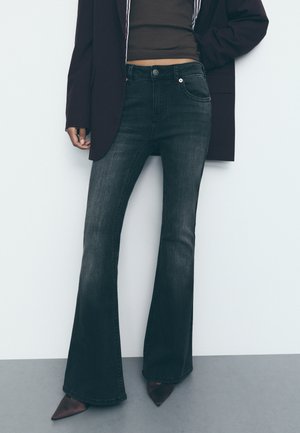 Dark wash flared jeans with a high waist, subtle pocket stitching, and a smooth texture, paired with pointed toe shoes and a blazer.