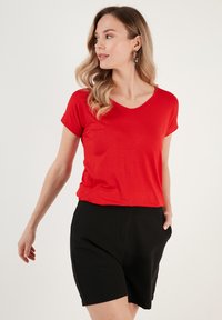 Rød kortærmet V-hals T-shirt med en afslappet pasform, parret med sorte shorts. Blødt stof med en glat tekstur. Ingen bemærkelsesværdige mønstre eller dekorationer.