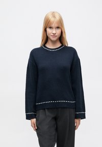 Pull-over bleu marine en matière douce, avec un col rond et des détails de couture blanche à l'ourlet et aux manches.