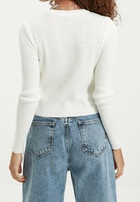Pull blanc côtelé à manches longues, taille cintrée et col rond, associé à un jean en denim bleu taille haute avec poches arrière.