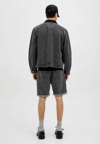 Veste en denim gris avec un col noir, associée à un short gris retroussé. Une casquette et des chaussures noires complètent la tenue. Design simple et dépouillé.