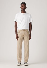 Beige denim jeans met een rechte pasvorm, gecombineerd met een plain wit katoenen T-shirt. Zwart-witte sneakers maken de outfit compleet.