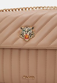 Sac à main en cuir matelassé beige avec bandoulière chaîne dorée, ornement tête de tigre dorée aux yeux verts, et logo ALDO en lettres dorées.