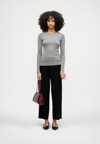 Γκρι ριγέ μπλούζα με μακριά μανίκια, συνδυασμένη με μαύρο παντελόνι σε φαρδιά γραμμή. Κρατάει μία μπορντό τσάντα χειρός και φοράει μαύρα παπούτσια με μυτερές μύτες.