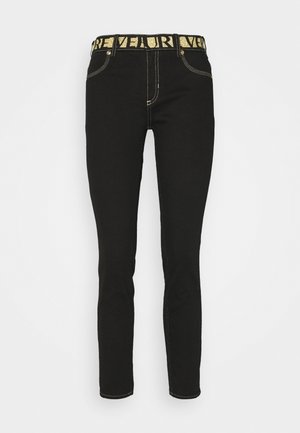 Pantalon noir ajusté avec des surpiqûres jaunes contrastantes et une large ceinture noire avec un texte jaune audacieux.