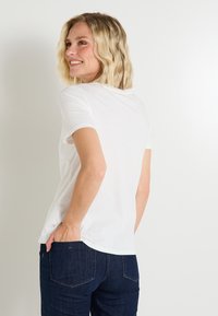 Camiseta blanca de manga corta, hecha de un tejido suave, con un sencillo escote redondo. Combinada con jeans de mezclilla oscura y un corte relajado.