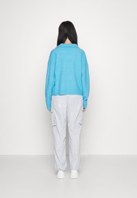 Hellblauer Pullover mit Kragen und geripptem Saum, kombiniert mit hellgrauen Cargo-Hosen mit Seitentaschen, getragen mit weißen Turnschuhen.