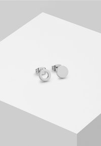 Silberne Metalldesign Ohrstecker mit einem kreisförmigen Diskus und einem offenen Kreismuster. Glatte Textur mit Hochglanz-Oberfläche.