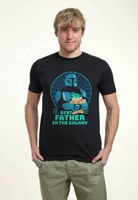 Black cotton t-shirt featuring a graphic print of a character holding a creature, with text "Best Father in the Galaxy" in teal and beige.