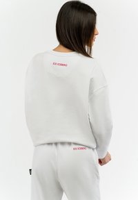 Felpa bianca e pantaloni abbinati in tessuto morbido. Presenta il testo rosso "ICE ICEBERG" sulla schiena della felpa e sui pantaloni.