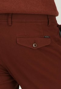 Bruine textuur broek met een achterzak met knoopsluiting en een merketiket, die een getailleerd ontwerp en stevige materialen laat zien.