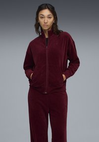 Burgundy corduroy zip-up jacket with front pockets, paired with matching pants. Features ribbed texture and subtle logo detail.