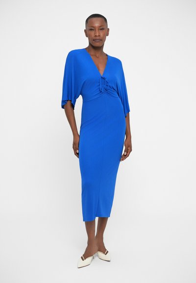 Modra obleka slim fit z V-izrezom in krilastimi rokavi. Mehak material se gladko pada, s poudarjeno podrobnostjo na pasu.