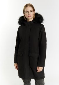 Sort lang parka-frakke med en foring af pels i hætten, der har en foran lynlås, to forlommer og et glat, tekstureret stof.