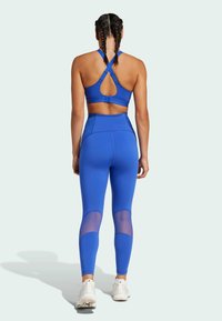 Modrý atletický crop top s prekríženými ramienkami a výrezom na chrbte, kombinovaný s legínami s vysokým pásom s priedušnými sieťkovanými panelmi na lýtkach.