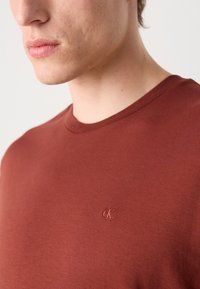 Tricou burgundy cu guler rotund, fabricat din bumbac moale, cu o textură subtilă, având un mic logo brodat pe pieptul stâng.