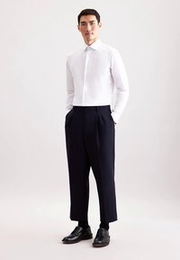 Witte blouse met knopen, marineblauwe geplooide broek, zwarte nette schoenen, slim fit, gladde textuur, op maat gemaakt ontwerp met zichtbare naden en manchetten.