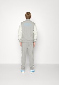 Grå Nike-sweatshirt med ljusgrå ärmar och blå logotyp på baksidan, i kombination med matchande grå joggingbyxor och ljusblå sneakers.