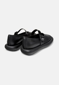 Zapatos de cuero negro con punta redondeada, correa trasera y diseño minimalista. Cuentan con una suela gruesa y acolchada para mayor comodidad.