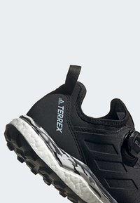Chaussure de trail running Adidas Terrex noire avec semelle texturée, languette de tirage au talon et système de laçage à disque BOA.
