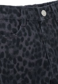 Gros plan sur un jean en denim noir avec un motif léopard sombre subtil, montrant la poche avant, la passante de ceinture et le bouton argenté.
