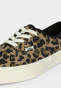 Baskets basses Vans avec un imprimé léopard beige et noir, lacets blancs, œillets métalliques et semelle en caoutchouc blanche.