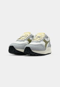 Grey suede sneakers with olive green accents, textured rubber outsole, cream laces, and yellow logo tag on the tongue.
