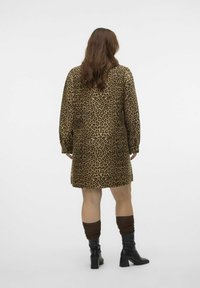 Haljina s uzorkom leoparda u smeđim i crnim nijansama, s dugim rukavima i širokim krojem, do sredine butina. Uparena s crnim čizmama do koljena i smeškim čarapama.