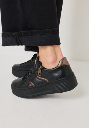 Sneakers in pelle nera con accenti metallici, chiusura con lacci e cerniera, suola piatta testurizzata e motivo di battistrada visibile.