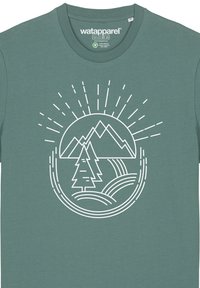 Teal katoenen t-shirt met een wit grafisch ontwerp van bergen, een boom en zonnestralen, gecentreerd op de voorkant. Zachte textuur.