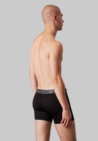 Sorte boksershorts med en glat tekstur, med en grå talje. Designet er tætsiddende og strækker sig til midt på låret.