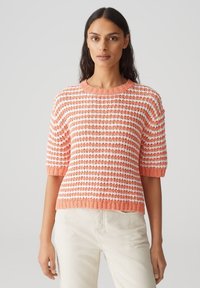 Pull à manches courtes rayé corail et blanc, texture tricotée, col rond, coupe légèrement ample, ourlet et accents de poignets côtelés.