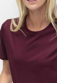 Burgundin värinen puuvillapaita, jossa on lyhyt hiha ja pyöreä pääntie. Kangas näyttää sileältä, ja siinä on vain vähäistä tekstuuria ilman näkyviä kuvioita tai yksityiskohtia.