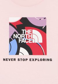 Το λογότυπο της The North Face με αφηρημένα κόκκινα, μοβ, μαύ ρα και μπλε σχήματα και τη φράση «Ποτέ μην σταματάς να εξερευνάς» σε ανοιχτό ροζ φόντο.