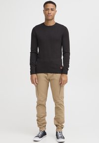 Svart genser i strikk med lange ermer, kombinert med beige cargo-bukser og svarte høyhælte sneakers. Genseren har rund halsringning og ribbestrikket kant.