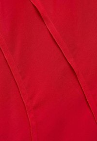 Tela roja con una textura suave, que presenta pliegues marcados creando un diseño drapeado. Se pueden ver líneas de costura sutiles en la superficie.