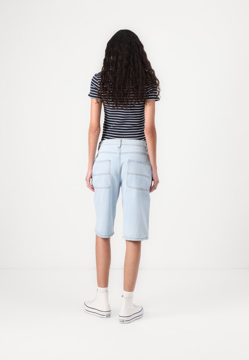 Shorts en denim bleu clair avec une coupe droite, dotés de poches arrière et d'ourlets retroussés, associés à un haut rayé bleu marine et blanc.
