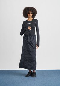 Čierny top s dlhým rukávom s bielym prešívaním, v kombinácii s čiernou sukňou dĺžky do členkov a čiernymi teniskami. Malá čierna kabelka nosená cez rameno.