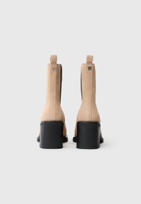 Μπεζ σουέτ ankle boots με μαύρους μπλοκ τακουνιών, που διαθέτουν πλαϊνές ελαστικές πάνελ και θηλιές για εύκολη εφαρμογή. Λεπτομέρεια λογότυπου στο πίσω μέρος.