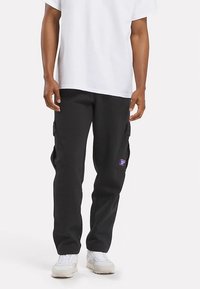 Črne hlače za tovor z bočnimi žepi, narejene iz bombažne mešanice, s majhno logotipno značko na levi strani, kombinirane z belo majico in belimi supergami.