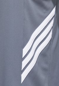 Shorts de sport gris en tissu respirant dotés de trois bandes blanches diagonales sur le côté, créant un élément de design élégant.