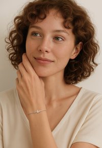 Bracciale in argento con un charm a forma di croce su una catena delicata, indossato al polso di una donna. Il bracciale presenta una finitura liscia e un design minimalista.