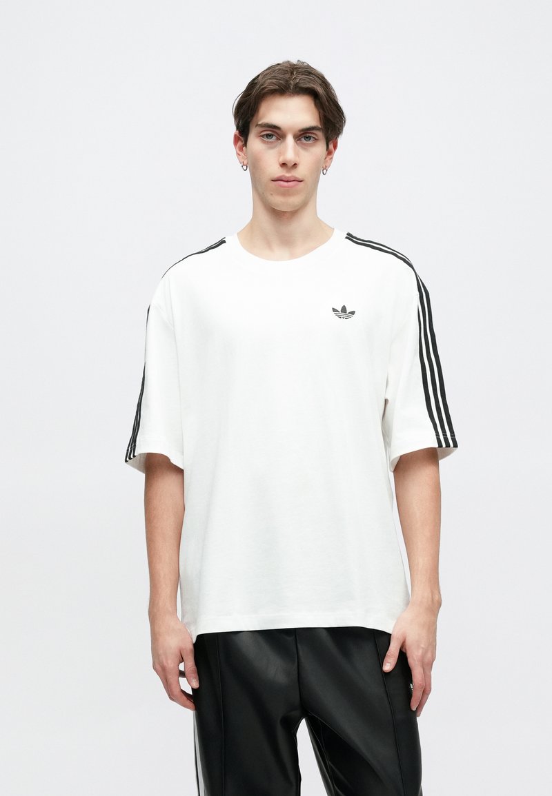 Short-sleeve white t-shirt made of cotton, featuring black three-stripe accents on the shoulders and a small logo on the chest.