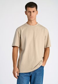 Beige puuvillane T-särk, ümarate kaelustega ja lühikeste varrukatega, koos siniste teksadega. Sile tekstuur ja lõdva lõikega.