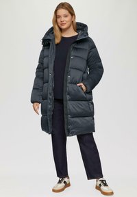 Lange, puffy, donkerblauwe parka met een capuchon, getextureerde panelen, drukknoopsluitingen en zijzakken, gecombineerd met donkere jeans en bicolore schoenen.