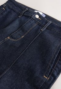 Blugi din denim albastru închis, cu design cu picior drept, prevăzuți cu buzunare standard, cusături contrastante și închidere frontală cu nasture vizibil.