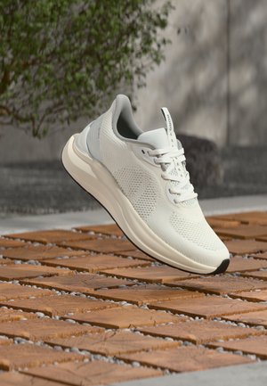 Pantof sport ușor, alb, cu partea superioară din plasă, talpă amortizată și șireturi, prezentat plutind deasupra unei suprafețe exterioare cu plăci.