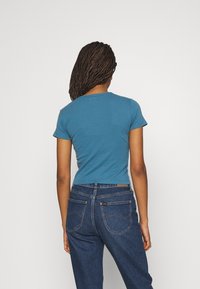 Blue short-sleeved cotton t-shirt with a round neckline, paired with high-waisted dark blue denim jeans featuring back pockets and stitching details.