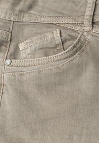 Tissu en denim beige montrant une poche avant avec une petite poche intérieure et un rivet métallique sur les coutures cousues.
