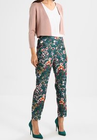 Ljusrosa kort cardigan över en vit topp, ihopparad med högmidjade blommiga gröna byxor och tealfärgade högklackade skor. Blomstertrycket har olika färger.